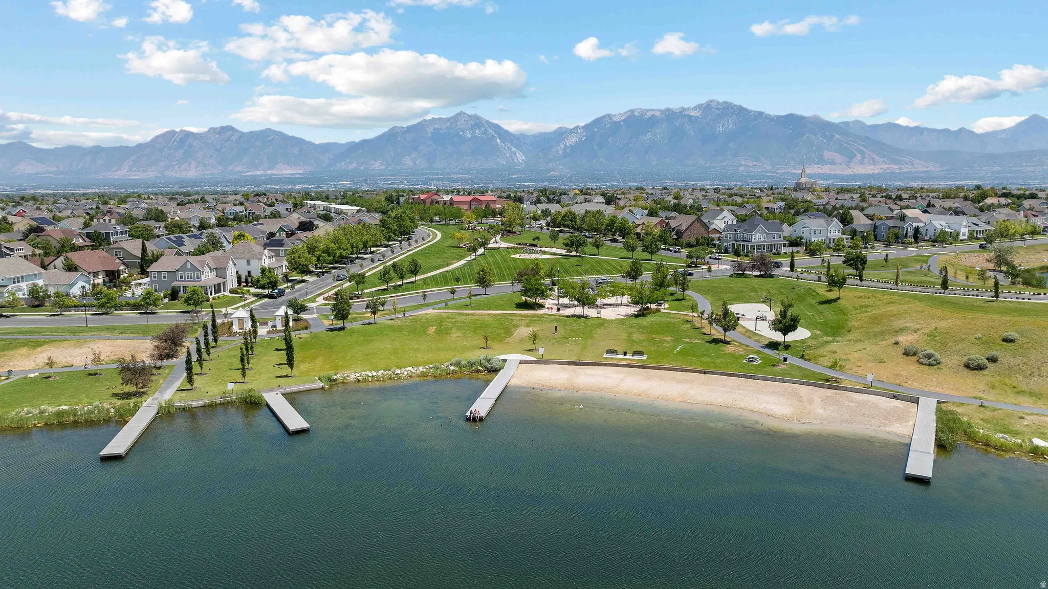 Lakeside property with multiple docks and a sandy shore, set against a backdrop of a residential neighborhood and distant mountains