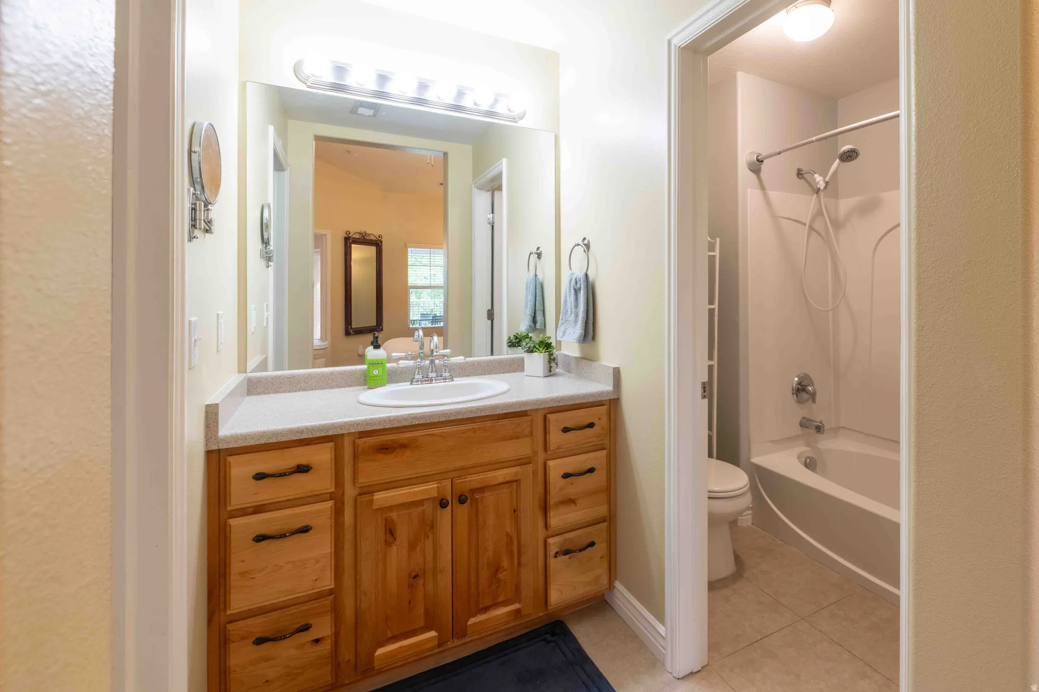 Bathroom vanity featuring a light wood-finish cabinet with multiple drawers and double-door storage, a light-toned countertop, and a large mirror