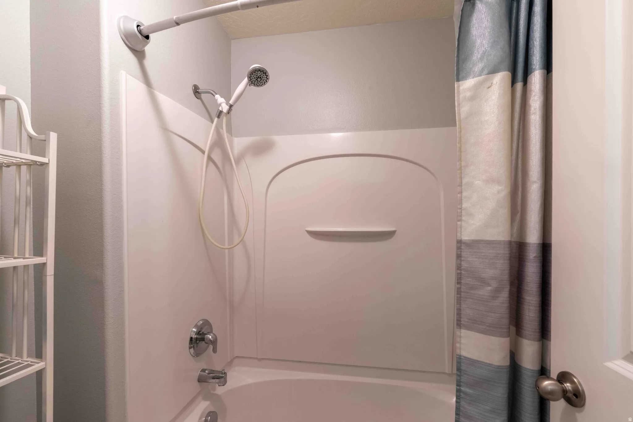 Tub and shower combination featuring an integrated shelf, a flexible handheld shower head, and polished chrome fixtures
