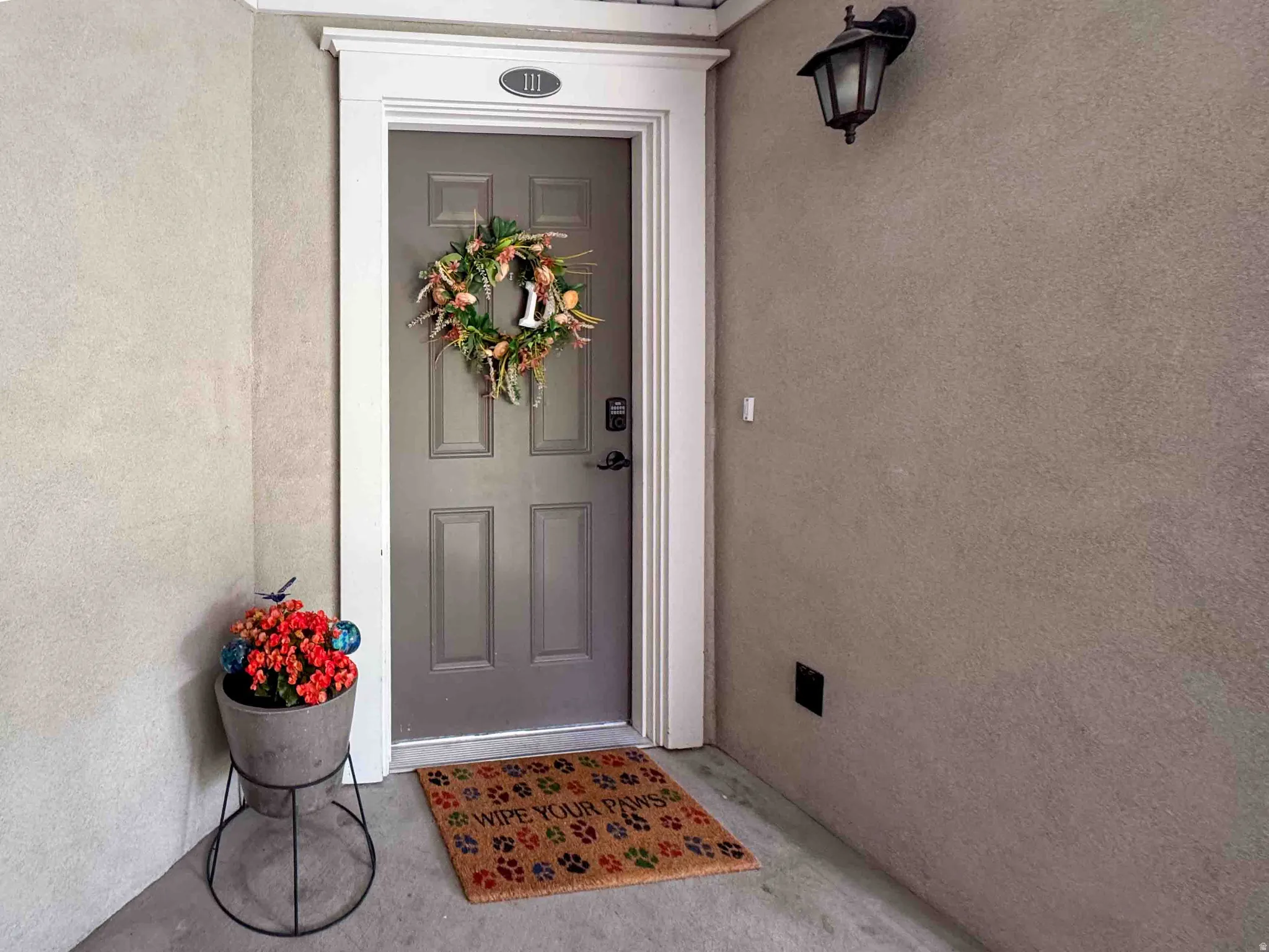 Grey paneled door with white trim, featuring an overhead exterior light fixture and stucco siding