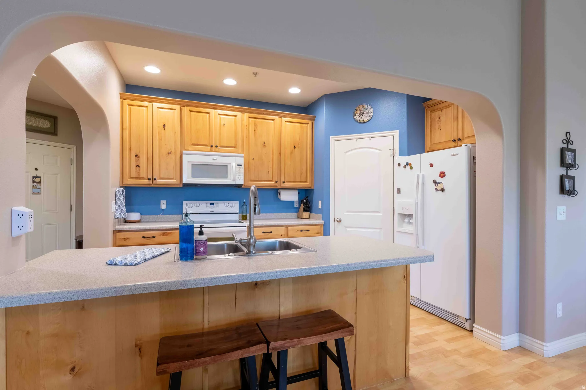 Kitchen featuring wood cabinetry, white appliances, a double basin stainless steel sink, and light countertops