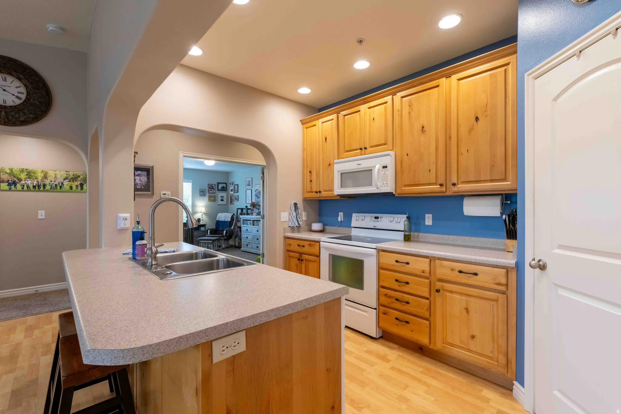 Kitchen featuring a double basin sink, light wood cabinetry, white appliances, and recessed lighting