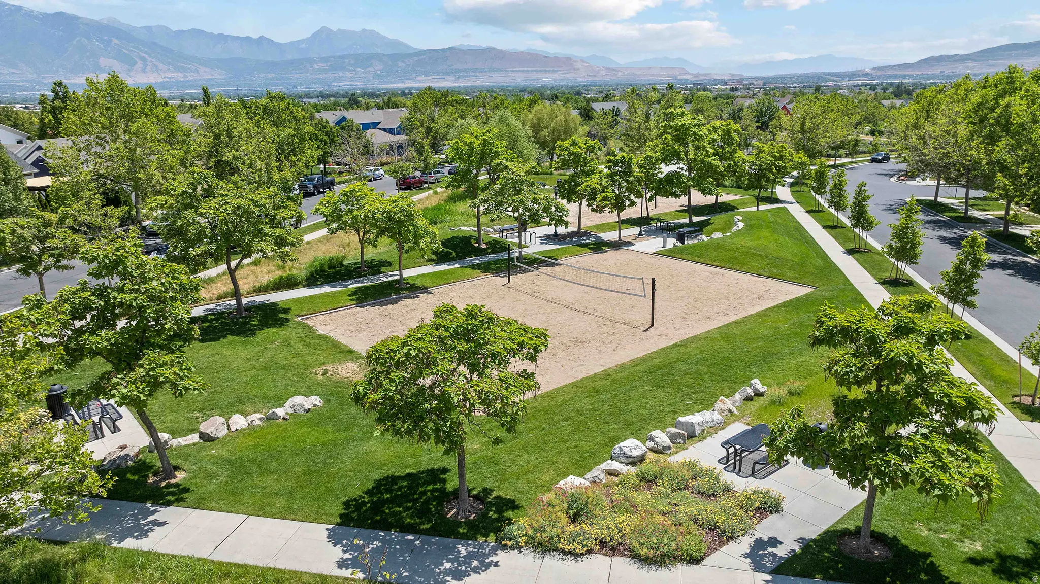 Community green space featuring a sand volleyball court, mature trees, and manicured lawns