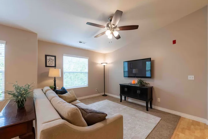 Living area featuring a vaulted ceiling with a ceiling fan, two large windows with blinds, and neutral-toned wall paint