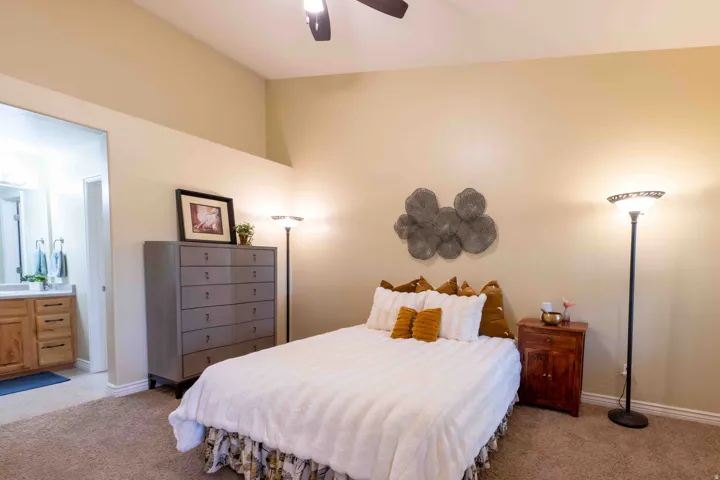 Carpeted room featuring a ceiling fan, vaulted ceiling, and an entry to a bathroom with a wood-finish vanity