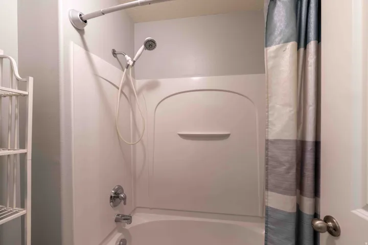 Tub and shower combination featuring an integrated shelf, a flexible handheld shower head, and polished chrome fixtures