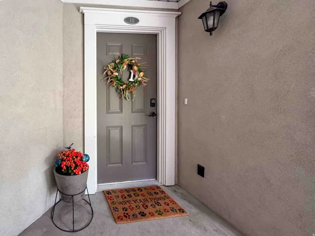 Grey paneled door with white trim, featuring an overhead exterior light fixture and stucco siding