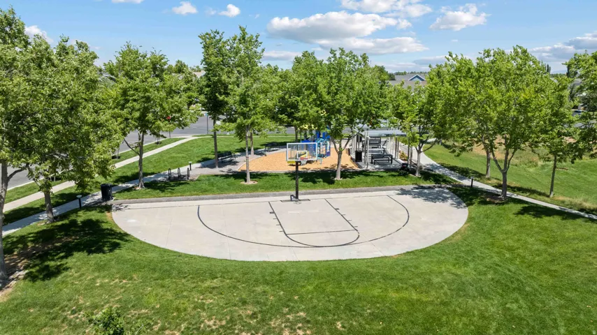 Expansive green space featuring a concrete half-basketball court, shaded gathering area with benches, and a playground structure