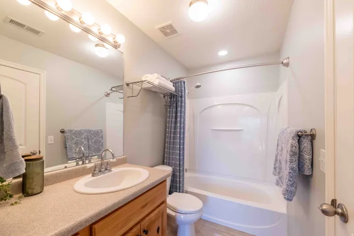 Bathroom with a light-toned countertop vanity, wood-finish cabinetry, built-in tub and shower combination, and overhead vanity lighting