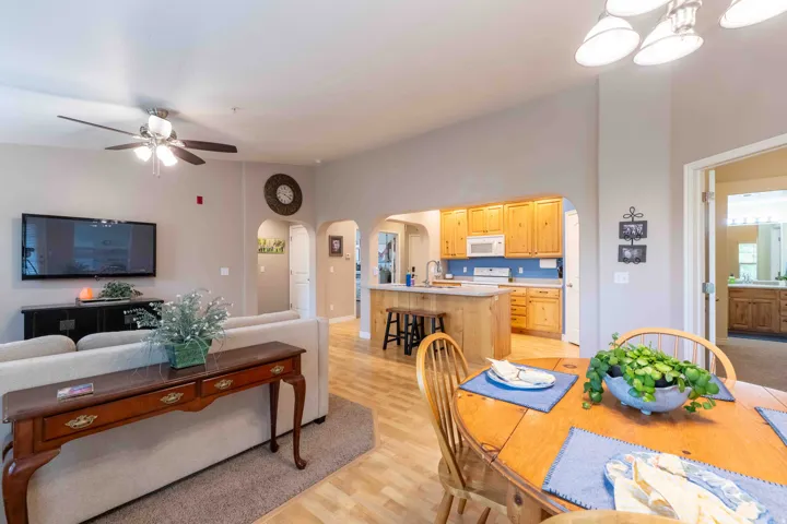 Open-concept living space featuring wood-finish flooring, a ceiling fan, and a kitchen with light wood cabinetry and a white microwave