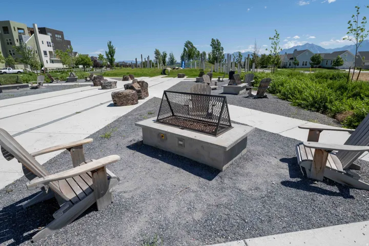 Outdoor gathering area featuring multiple concrete fire pits with metal grates, surrounded by Adirondack-style chairs