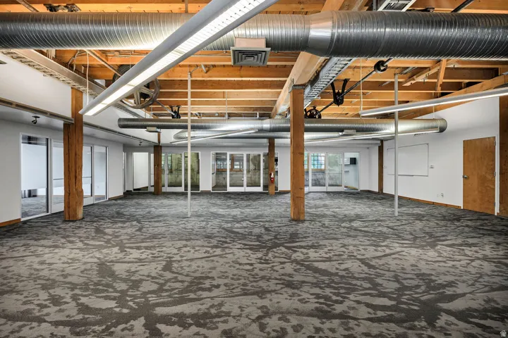 Expansive open-concept room featuring exposed wood ceiling beams, exposed metal ductwork, and patterned carpet flooring