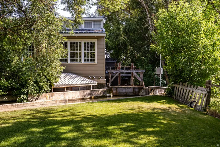 Spacious lawn with mature trees, featuring a building with extensive multi-pane windows, a pitched metal roof, and a water feature with visible wooden structures