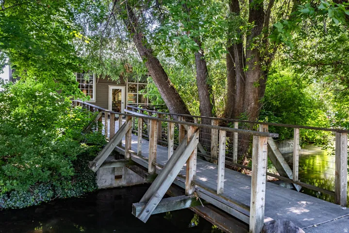 Wood-finish footbridge spanning a natural waterway, leading to an exterior entrance with a glass-paneled door