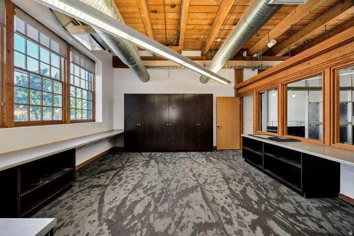 Open-concept interior featuring exposed wood beam ceilings, industrial-style ductwork, and large grid windows with wood framing