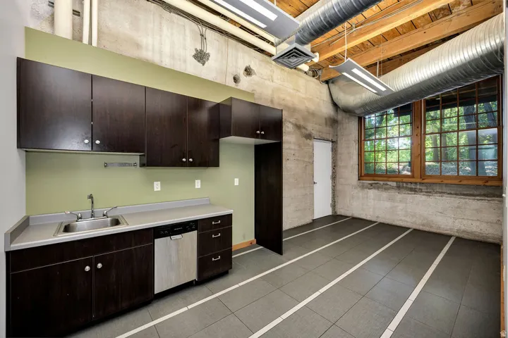 Industrial-style space featuring exposed concrete walls and ceiling, visible ductwork, and overhead fluorescent lighting
