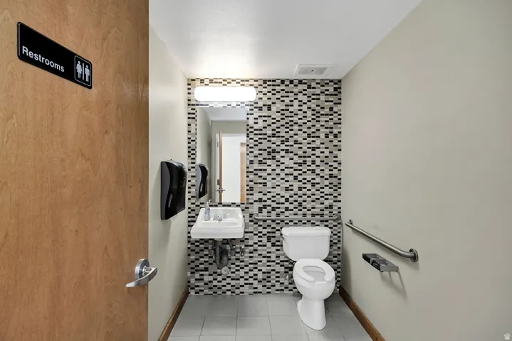 Restroom featuring a wall-mounted sink, toilet, and tile accent wall