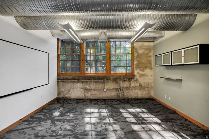 Industrial-style interior featuring exposed corrugated ductwork, large wood-framed windows, built-in wall cabinets, and patterned carpet flooring
