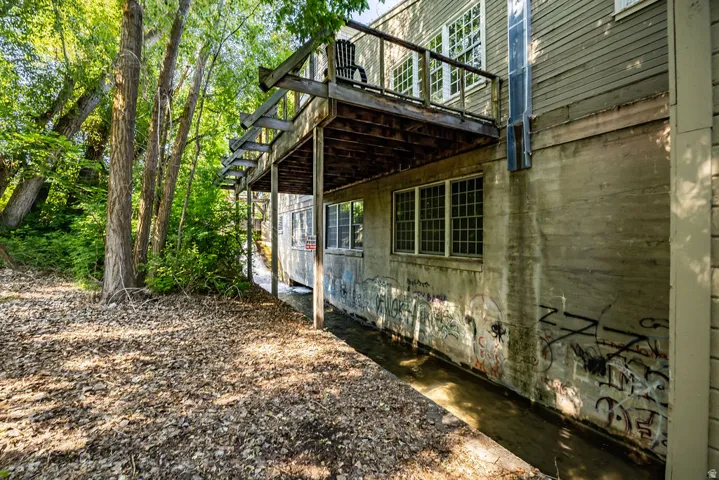 Lower-level concrete foundation with multiple grid-paned windows, bordered by a narrow water feature and dense mature trees
