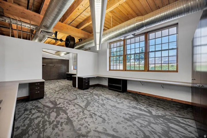 Open-concept commercial space featuring exposed wood beam ceilings, visible ductwork, and large grid-pattern windows