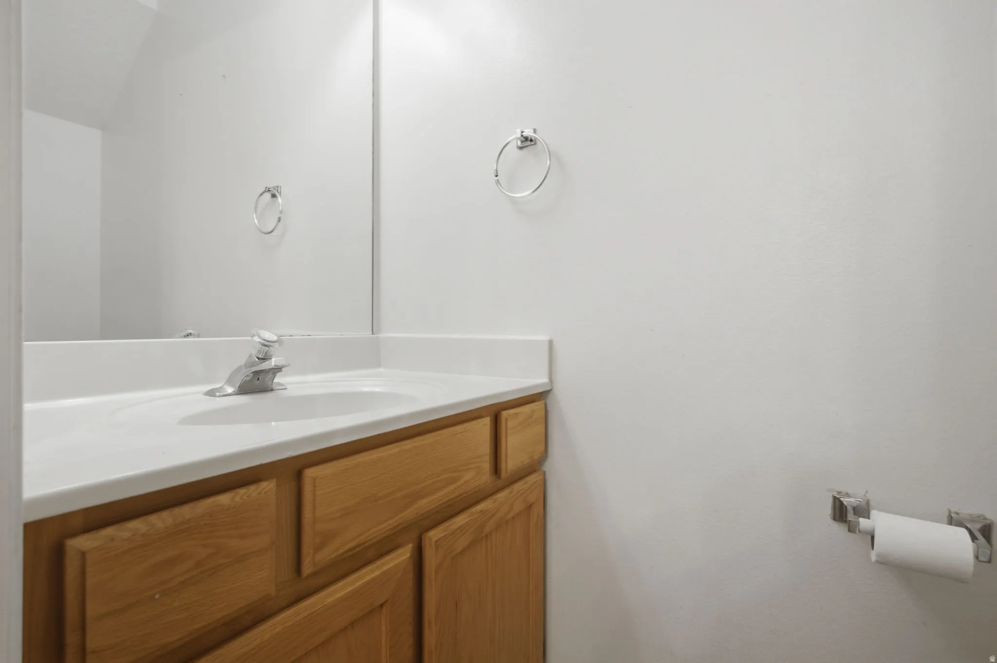 Bathroom vanity featuring a light wood-finish cabinet with panel doors, a white countertop with an integrated sink, and a chrome single-handle faucet