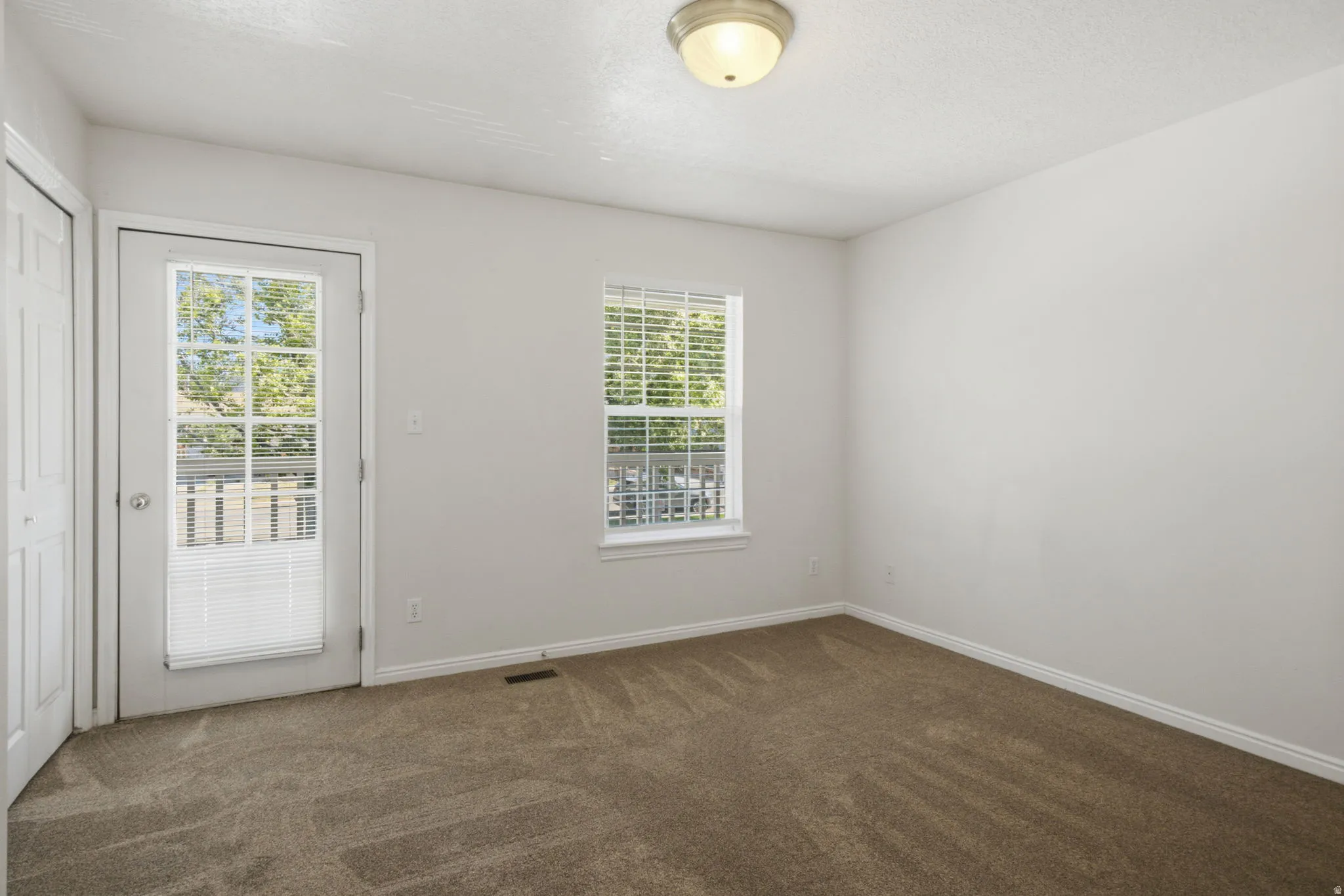 Carpeted room with a white door featuring full-light glass panels, a window with blinds, and white baseboards