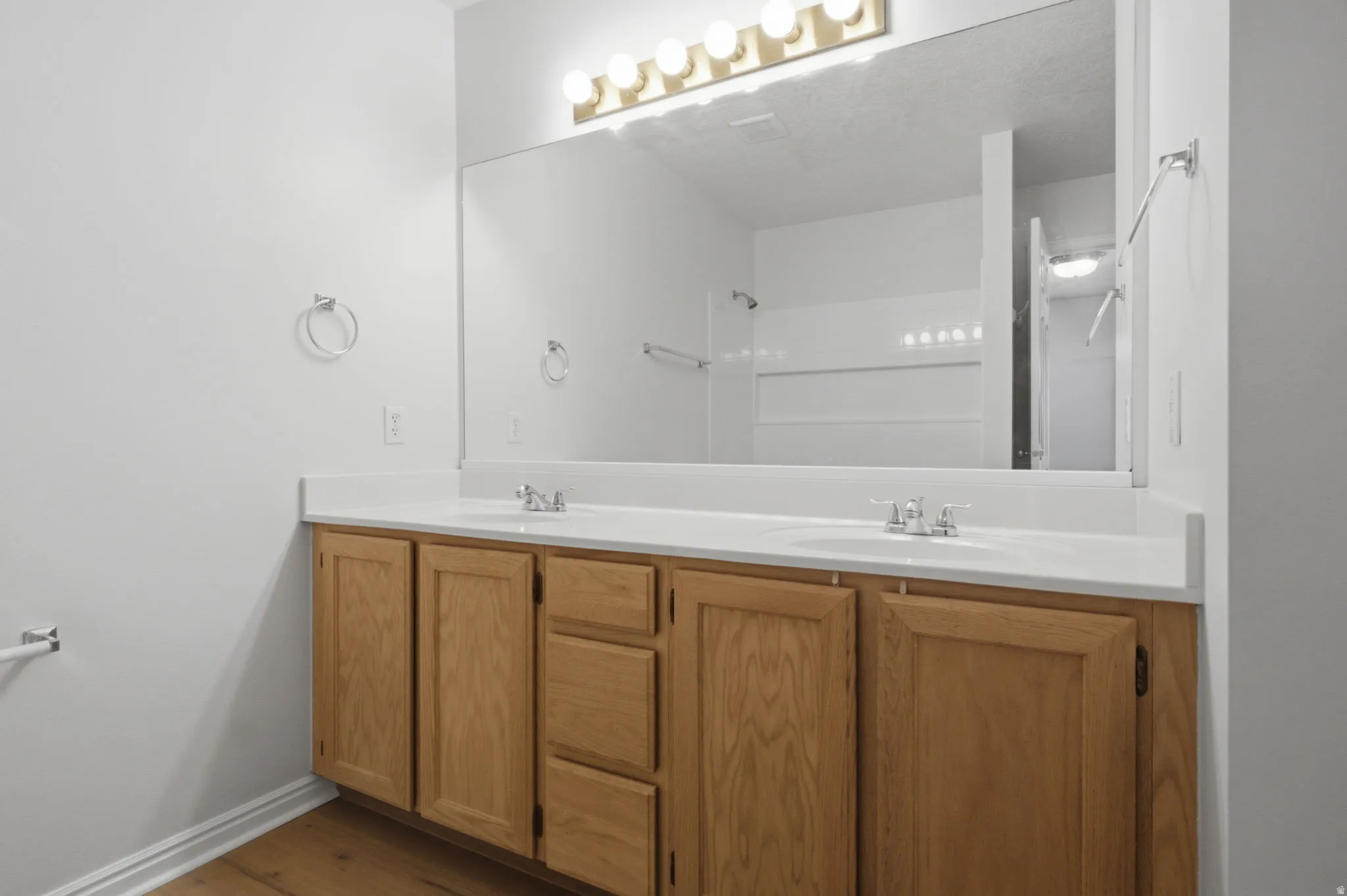 Double vanity with light wood cabinetry, white countertops, and chrome fixtures