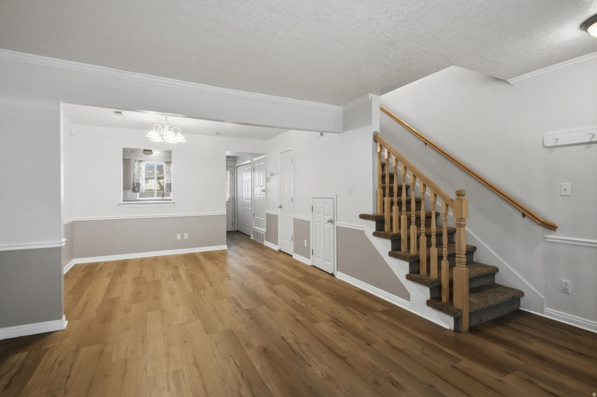 Open-concept living area with wood-finish flooring, two-tone painted walls, and crown molding