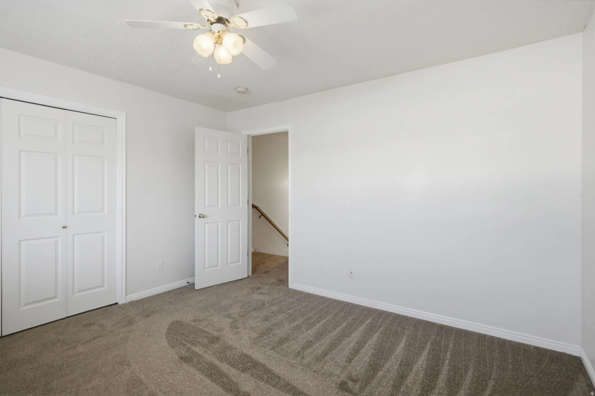 Neutral-toned carpeting in a room featuring a white ceiling fan with integrated lighting