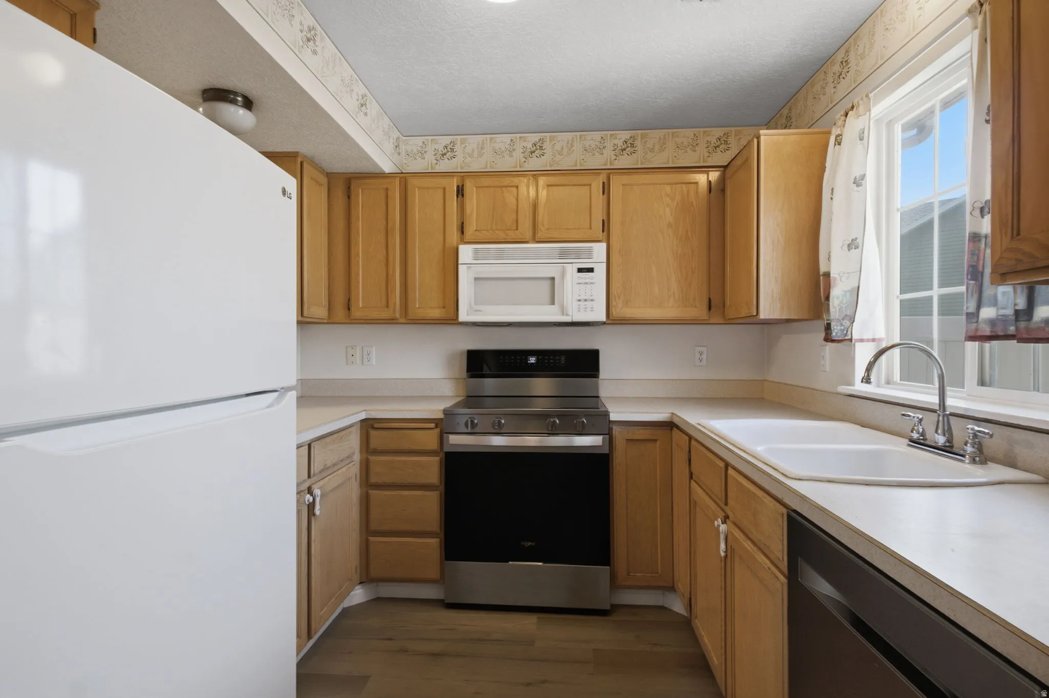 U-shaped kitchen layout featuring wood cabinetry, a stainless steel range, a built-in microwave, and a double basin sink beneath a window