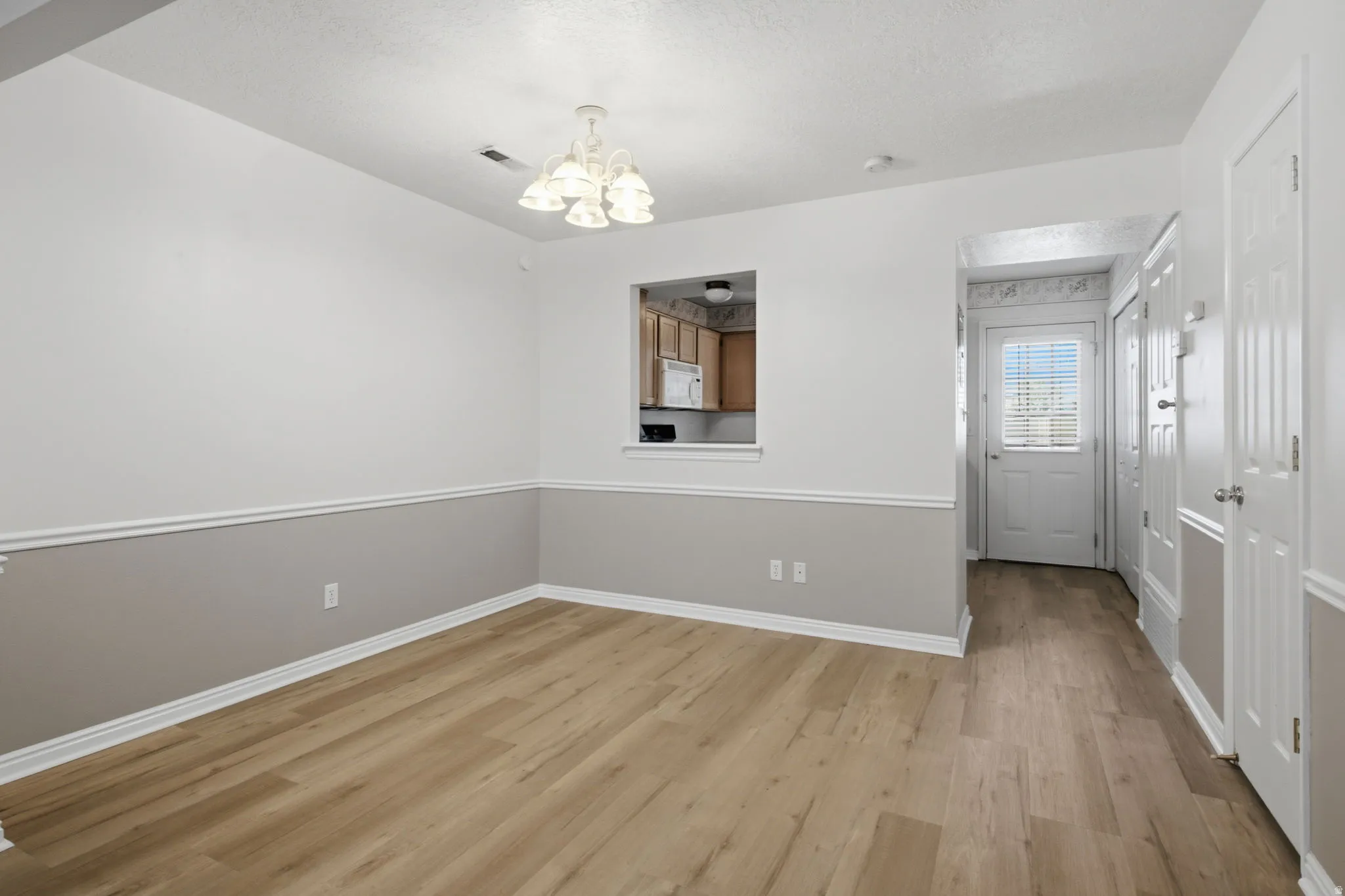 Dining area featuring wood-finish flooring, two-tone wall treatment, a ceiling-mounted chandelier, and a pass-through window to the kitchen