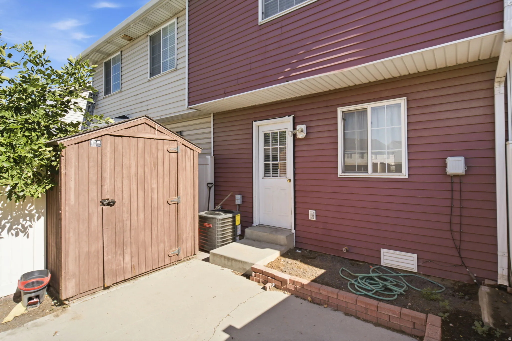 Private patio area featuring a storage shed, concrete pad, and brick-edged planting bed