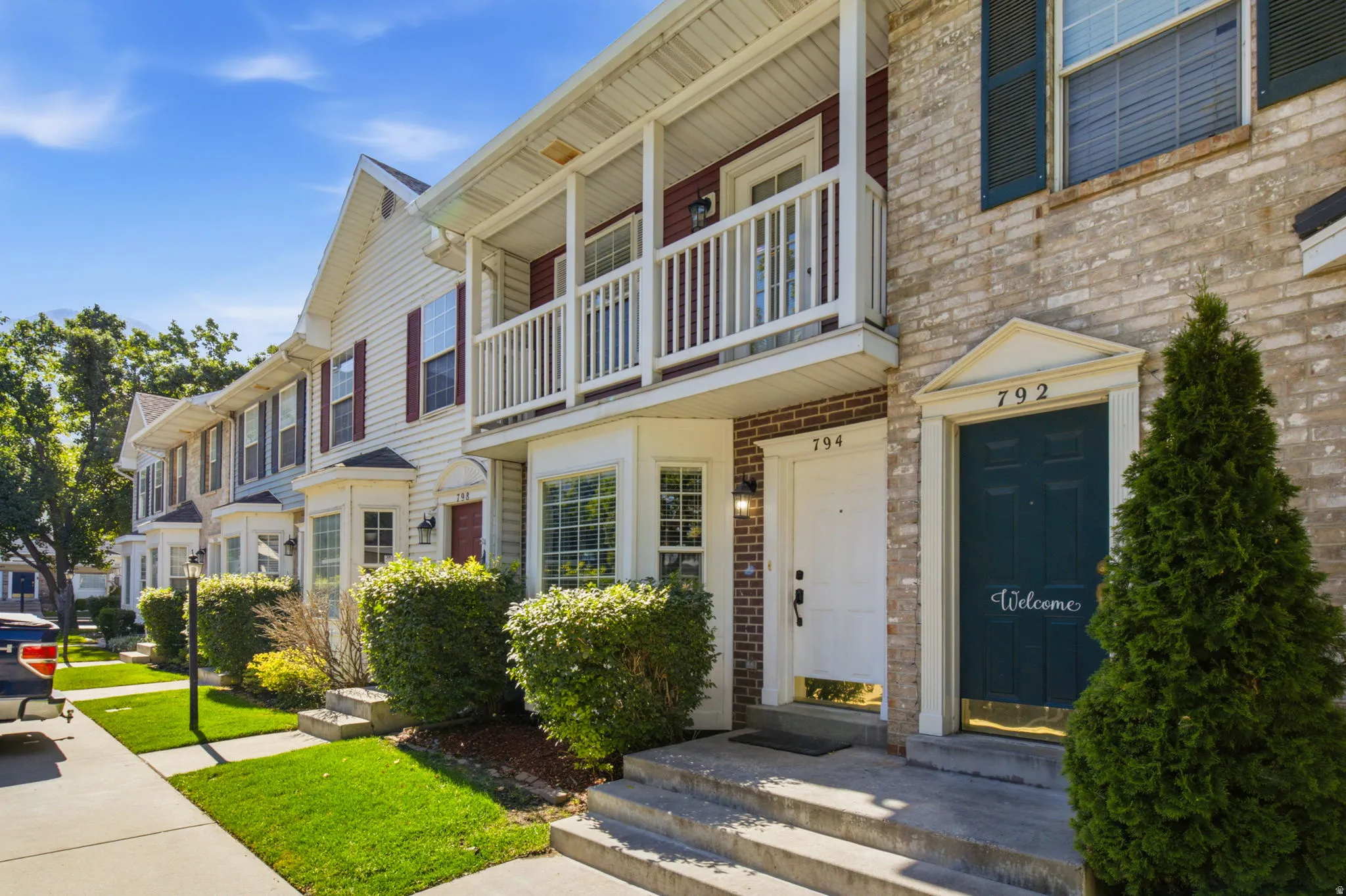 Traditional townhome exterior featuring a brick facade with shuttered windows, a white entry door with a transom window, and a second-story balcony