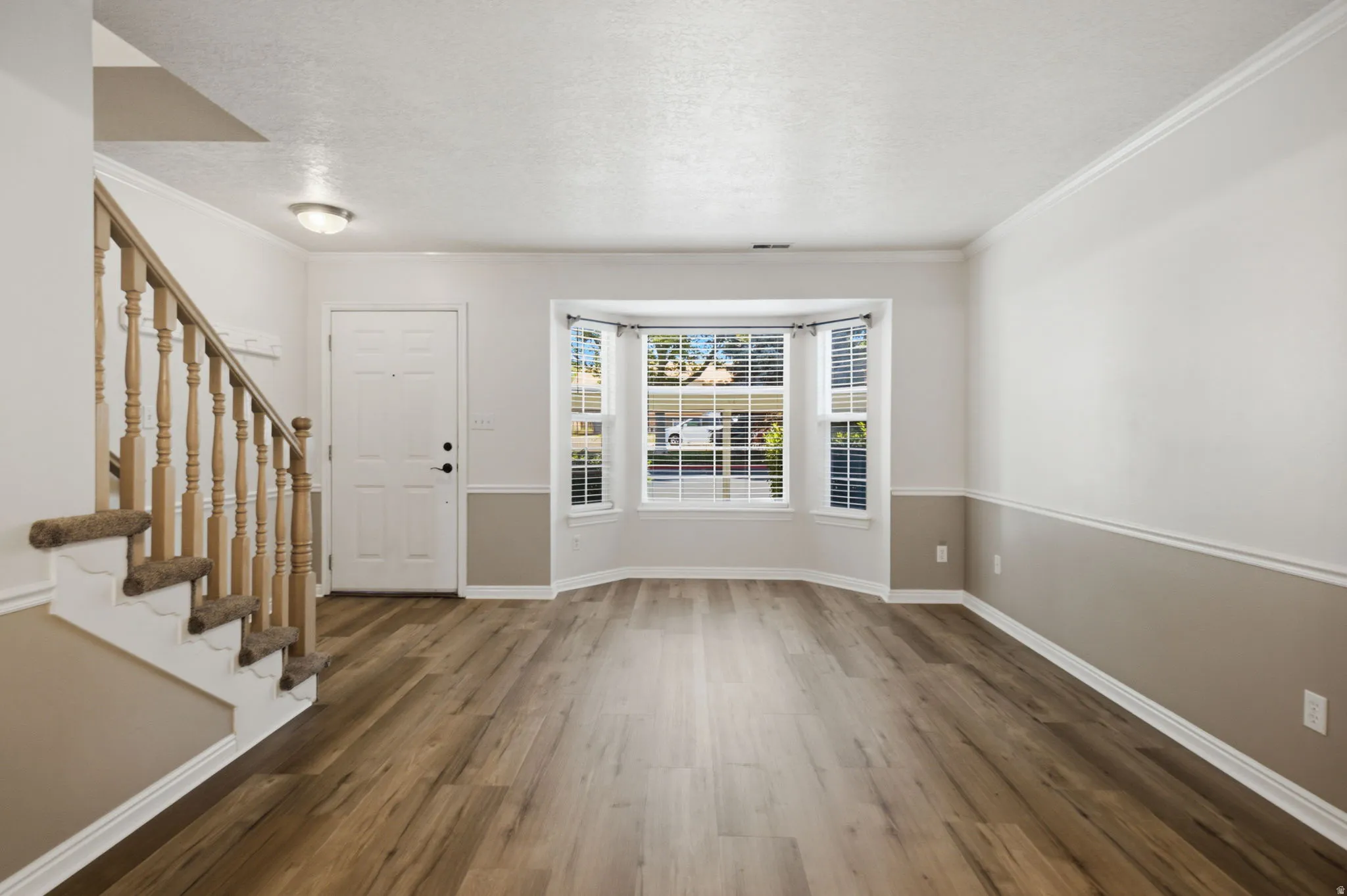 Entryway featuring wood-finish flooring, a bay window with blinds, and a staircase with wood newel posts and carpeted treads