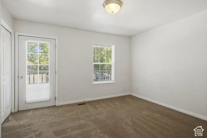 Carpeted room with a white door featuring full-light glass panels, a window with blinds, and white baseboards
