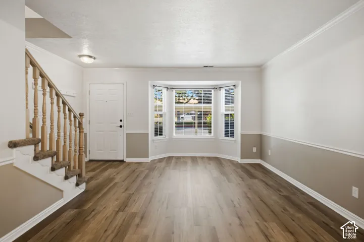 Entryway featuring wood-finish flooring, a bay window with blinds, and a staircase with wood newel posts and carpeted treads