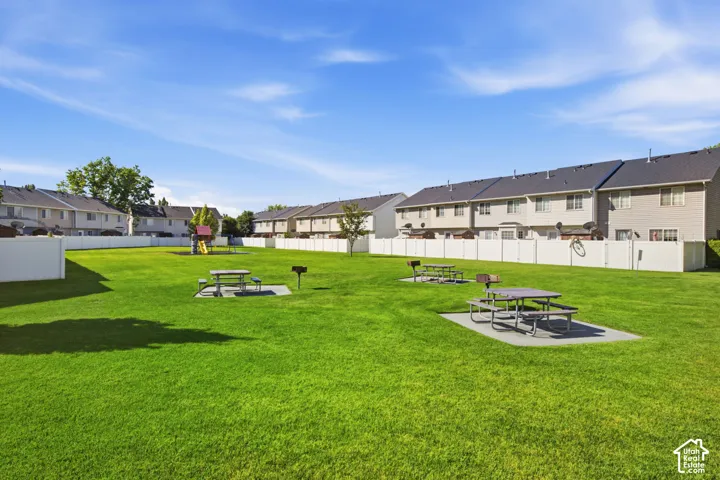 Expansive community green space featuring a manicured lawn, multiple picnic tables on concrete pads, built-in barbecue grills, and a dedicated play structure