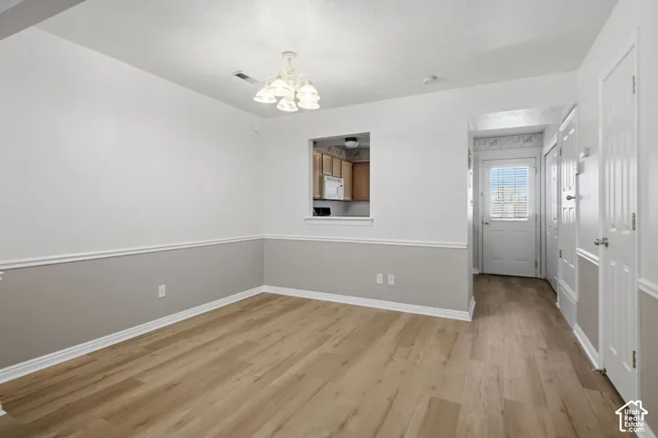 Dining area featuring wood-finish flooring, two-tone wall treatment, a ceiling-mounted chandelier, and a pass-through window to the kitchen