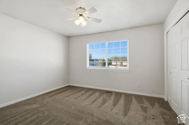 Spacious room featuring neutral carpeting, a large window, white trim, a ceiling fan with light fixture, and a bi-fold closet door