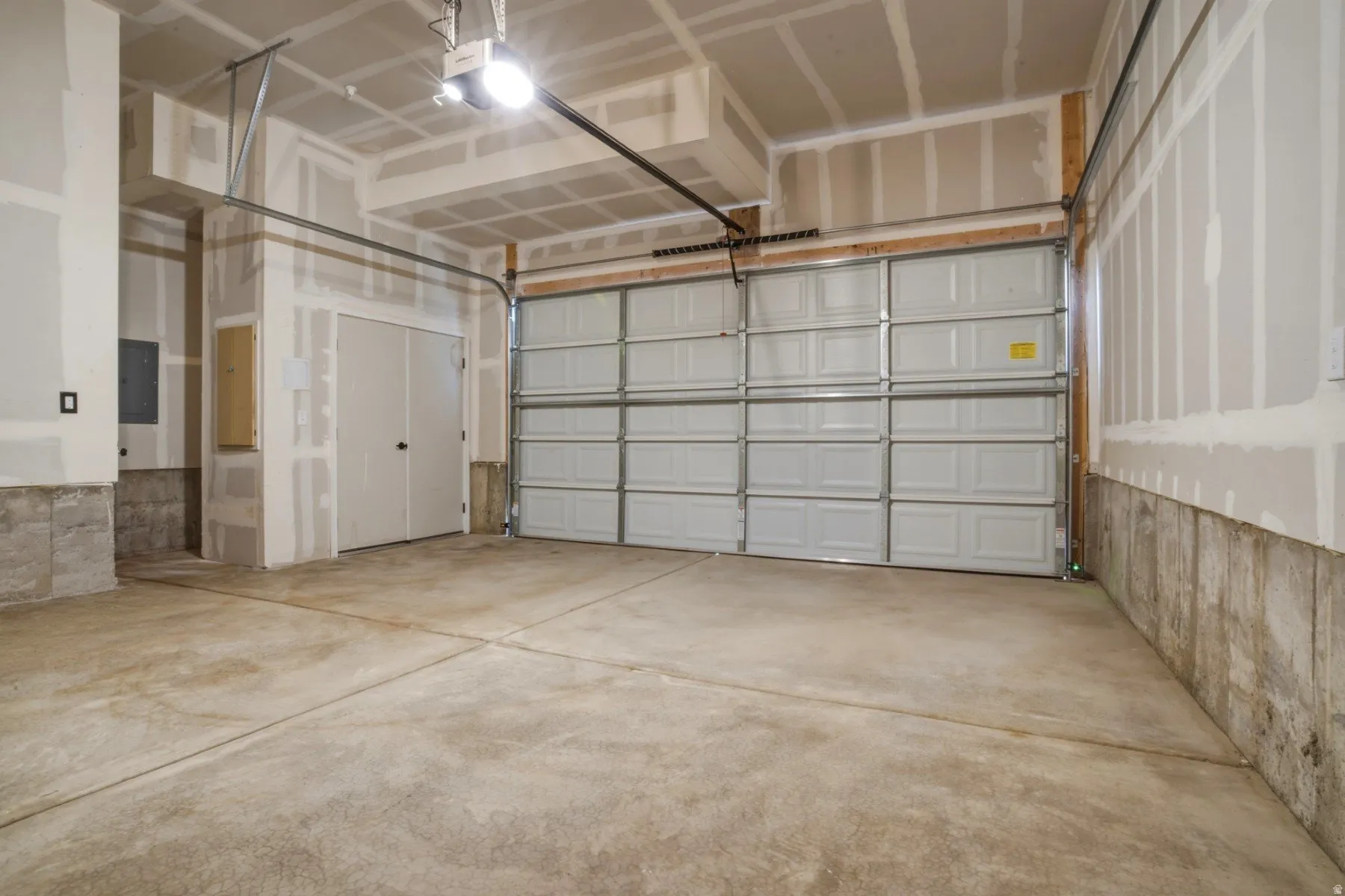Spacious interior garage featuring a segmented overhead door, concrete flooring, exposed studs and drywall, and a utility access panel