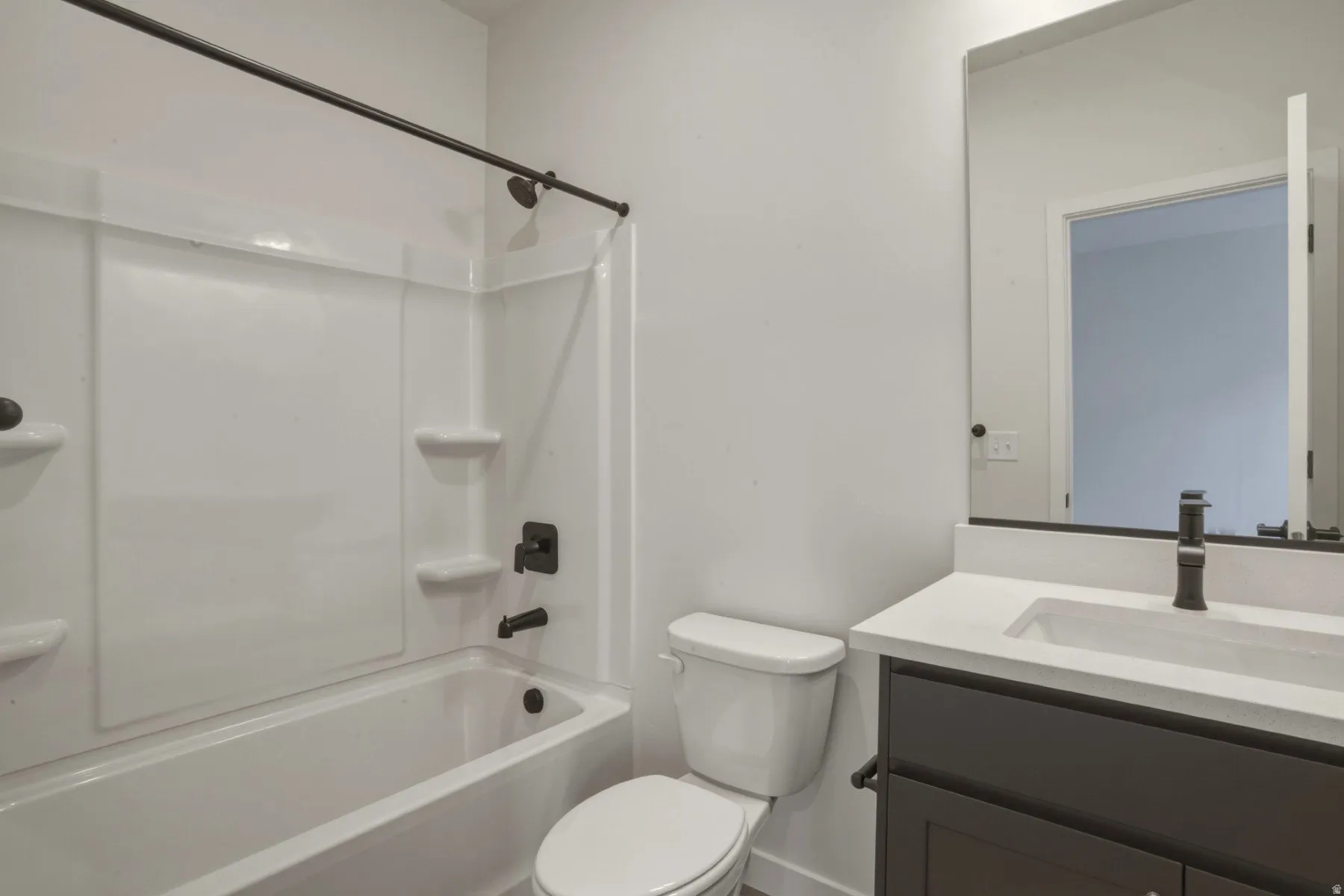 Bathroom featuring a white tub/shower combination with dark bronze fixtures, a dark brown vanity with a light countertop, an integrated sink, and a large wall-mounted mirror