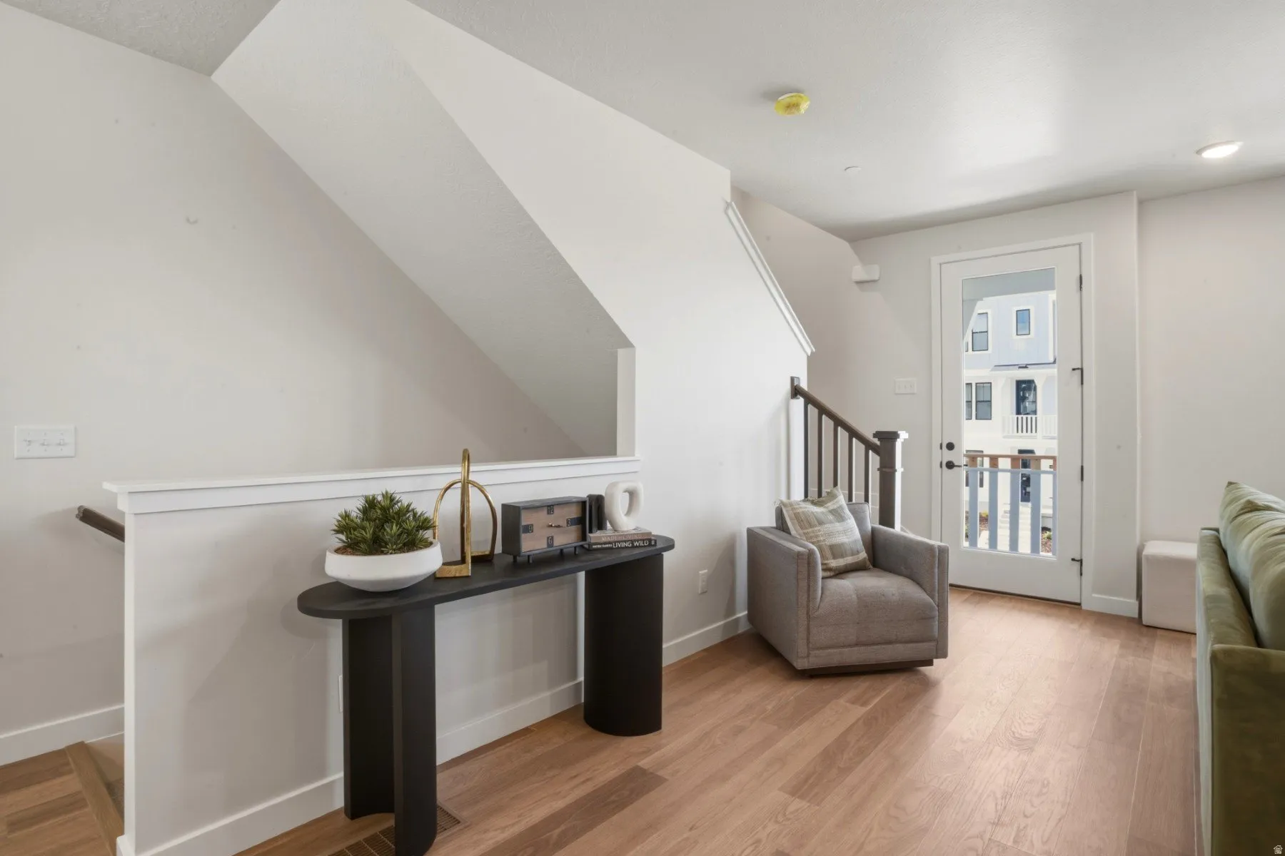 Bright living area featuring wood-finish flooring, a white glass-paneled door, and a staircase with dark wood newel posts and spindles