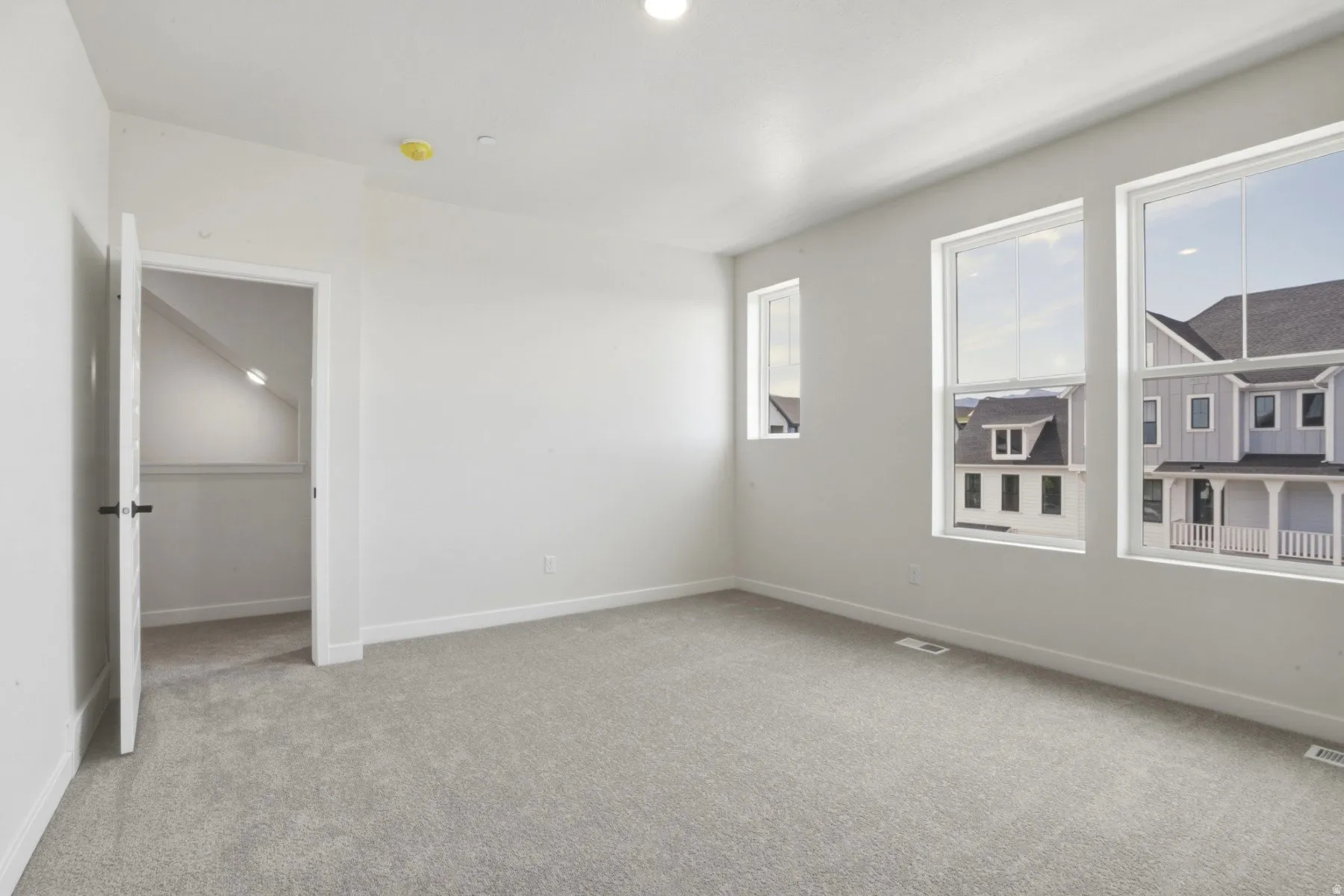 Bright room with light gray carpeting, crisp white walls, and three large windows providing abundant natural light