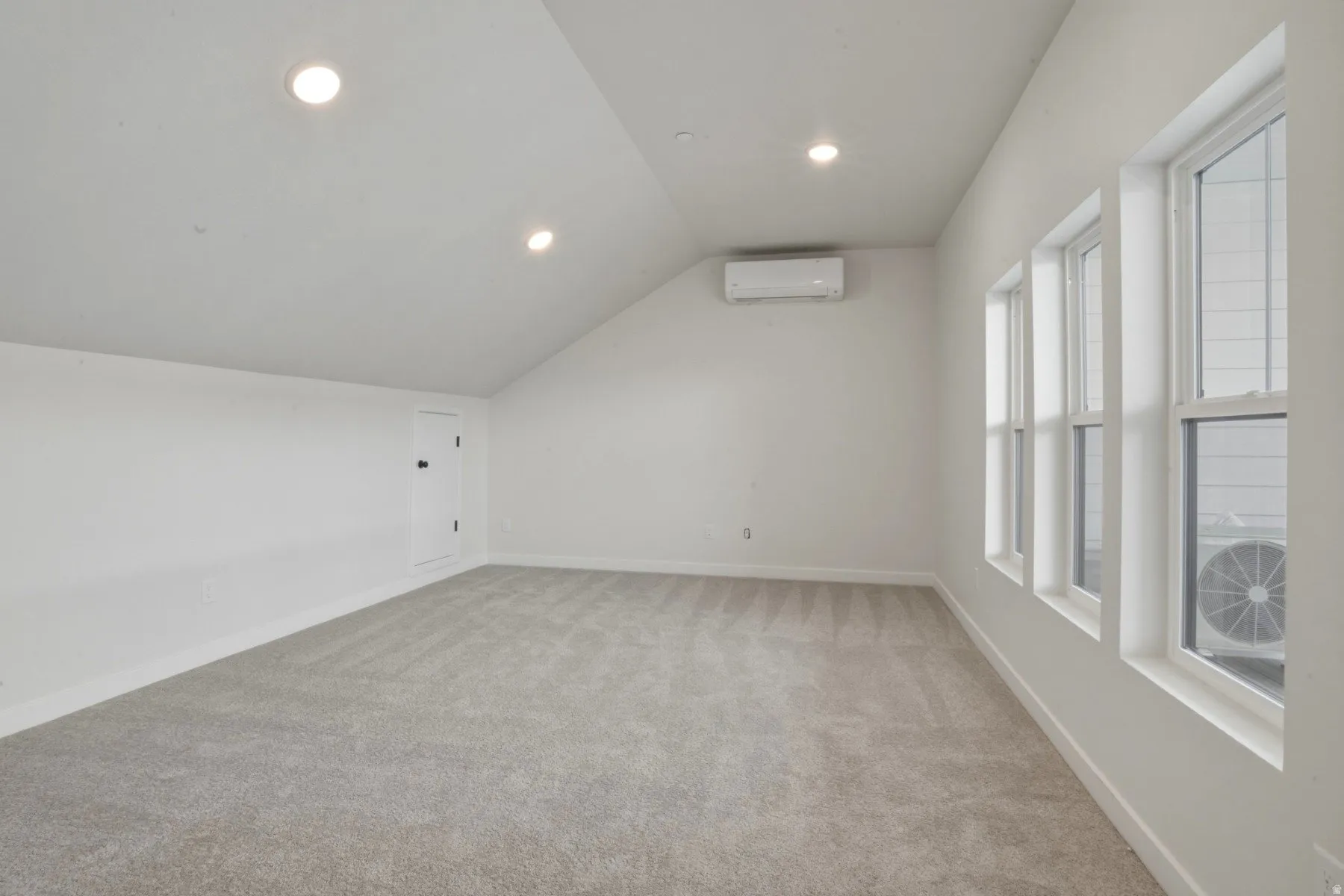 Carpeted room with multiple windows, recessed lighting, and a wall-mounted climate control unit
