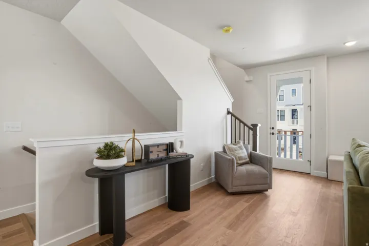 Bright living area featuring wood-finish flooring, a white glass-paneled door, and a staircase with dark wood newel posts and spindles
