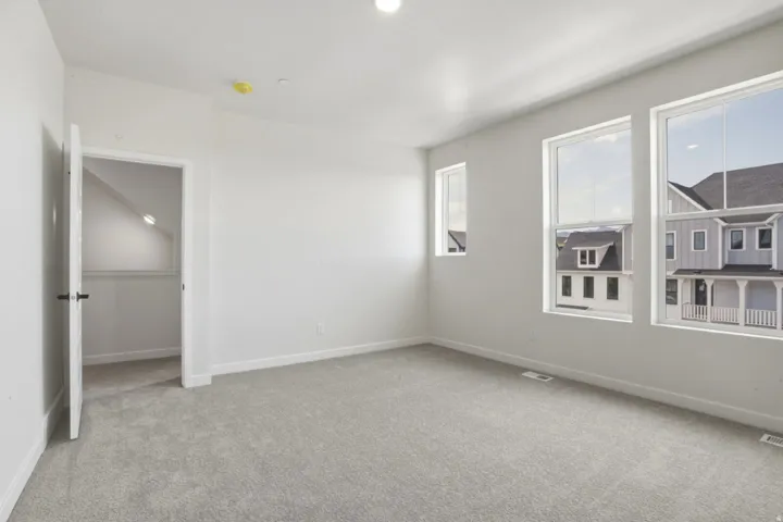 Bright room with light gray carpeting, crisp white walls, and three large windows providing abundant natural light