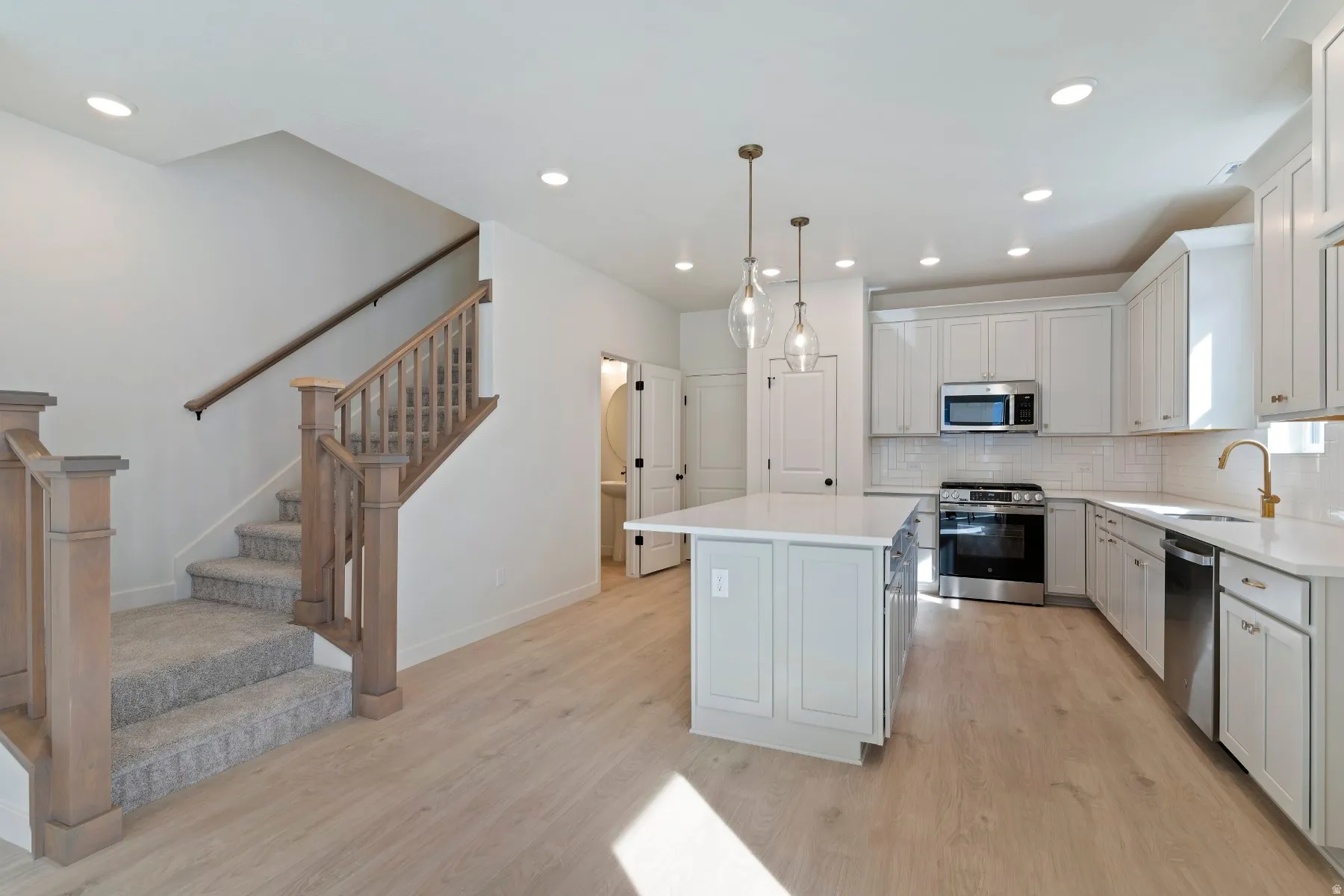 Open-concept kitchen featuring white shaker cabinetry, stainless steel appliances, a center island with seating, and pendant lighting