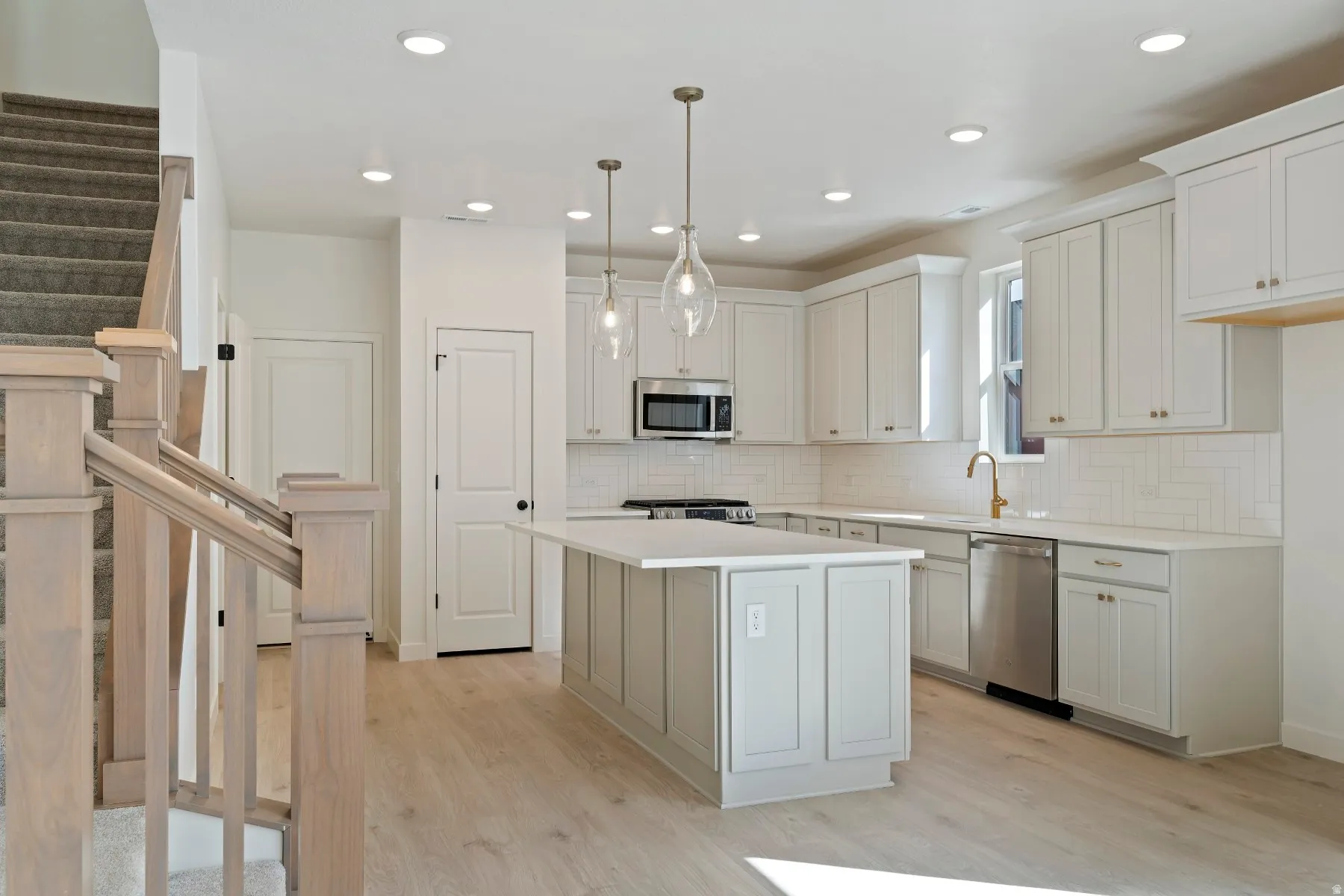 Bright kitchen featuring light wood-finish flooring, white cabinetry, a center island with pendant lighting, stainless steel appliances, and subway tile backsplash