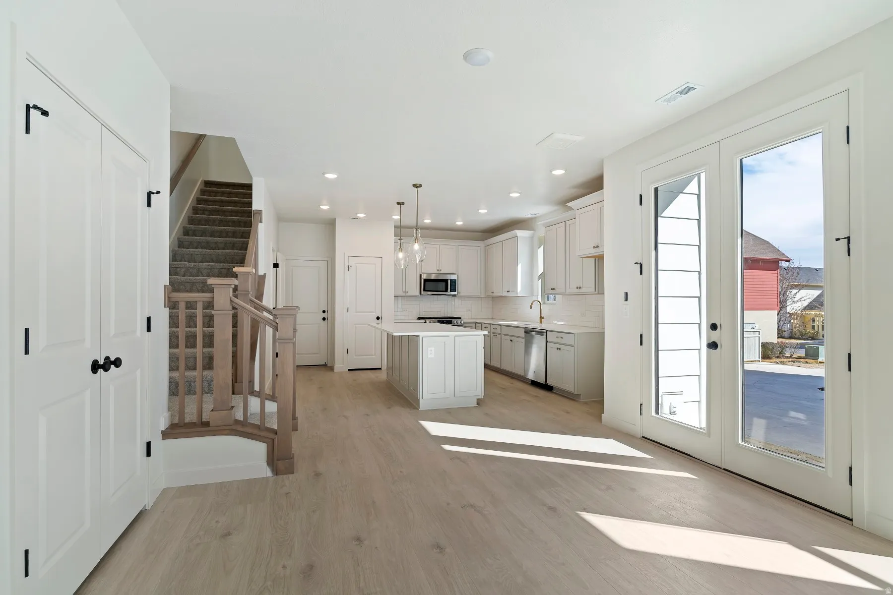 Open-concept living space featuring wood-finish flooring, a contemporary kitchen with a center island and pendant lighting, stainless steel appliances, and glass-paneled double doors