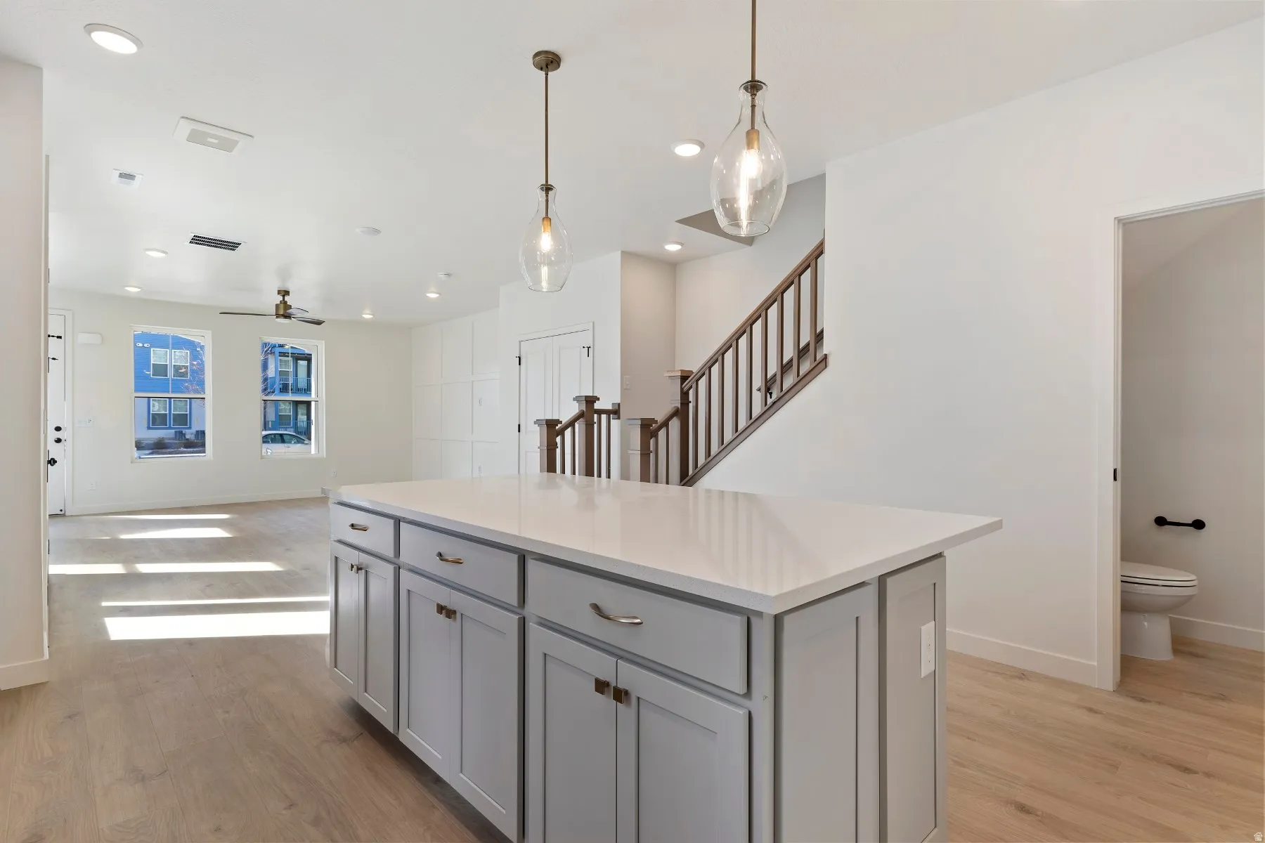 Kitchen island featuring light gray cabinetry, a white countertop, and two suspended pendant lights